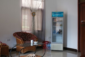 A living room with a wicker sofa, a glass coffee table, and a refrigerator. - Makeseni Lodge (Arusha)