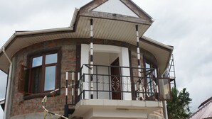 Um edifício com fachada de tijolos, uma varanda com guarda-corpo de metal e um telhado triangular.