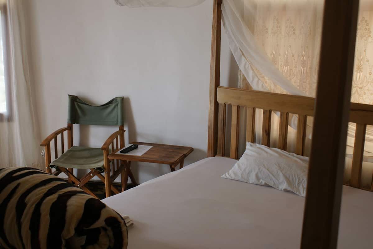 Un dormitorio con cama, una silla, una mesita y una cortina.