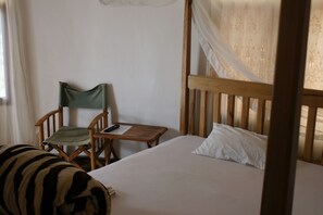 A bedroom with a bed, a chair, a small table, and a curtain. - Makeseni Lodge (Arusha)