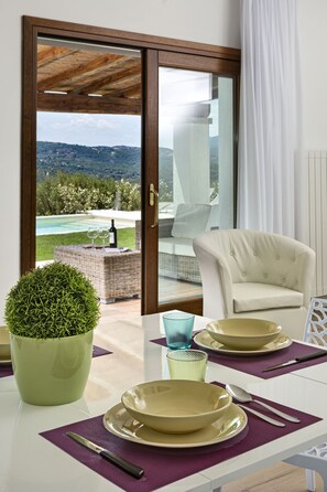 Ein Essbereich mit Tisch für zwei Personen, einem Blumentopf und Blick auf Pool und Berge durch eine Glastür.