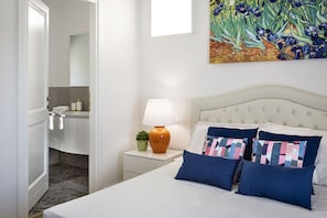 Ein Hotelzimmer mit Bett, Nachttisch, Lampe, einem Gemälde und einem durchgegangenen Tür erkennbaren Badezimmer.