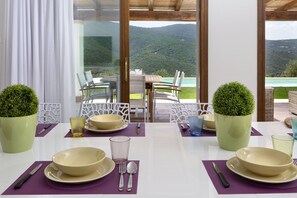 Ein Esstisch, gedeckt mit Tellern, Schüsseln, Besteck und Gläsern, mit Blick auf eine Berglandschaft.