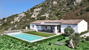 Eine weiße Villa mit Swimmingpool, Sitzgelegenheiten im Freien und einem Bergpanorama.