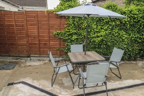 A patio with a table and chairs, an umbrella, a wooden fence, and a hedge. - Tí Maolla (Hollymount)