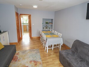 A dining area with a table set for six, a sofa, a rug, and a kitchen visible through an open door.