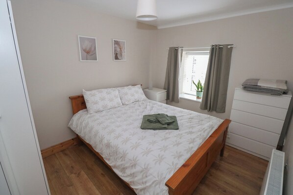 A bedroom with a bed, a nightstand, a window with curtains, a potted plant, and a dresser.
