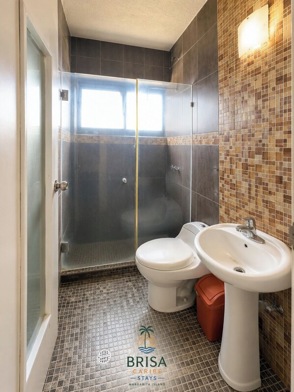 Une salle de bain avec une douche à parois de verre, deux toilettes blanches et un lavabo.