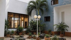 A modern building with multiple floors, large windows, and a courtyard with potted plants and a palm tree. - Modern 2 Bedroom apartment in Juangriego with Pool (Juangriego)