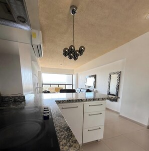 A modern kitchen with a central island, white cabinetry, and a large window providing natural light.
