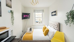 Una camera da letto con un letto, una poltrona gialla, una televisione e una finestra.