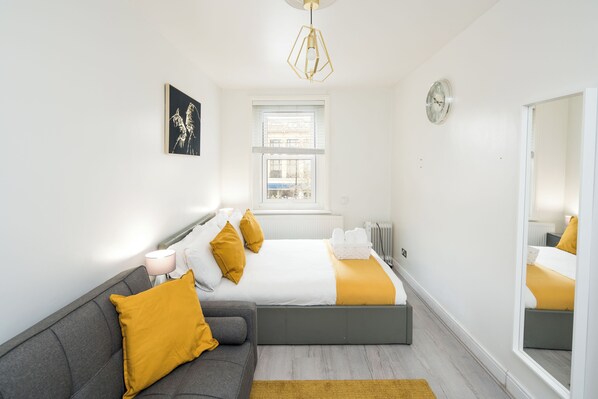 Une chambre à coucher moderne avec un lit, un canapé, une fenêtre et un miroir.