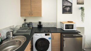 Una cucina compatta con lavatrice, forno a microonde, lavandino e mobili impiallacciati in legno.