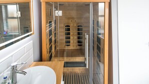 Un bagno moderno con sauna in vetro, lavandino bianco e mobile vanitario in legno.