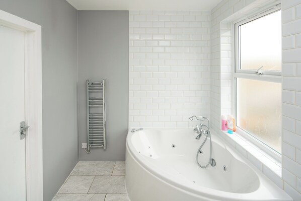 A bathroom with a white bathtub, a window, and a towel rack. - Stylish London Stay | Jacuzzi, Sauna & Near the City Up to 6 People (London)