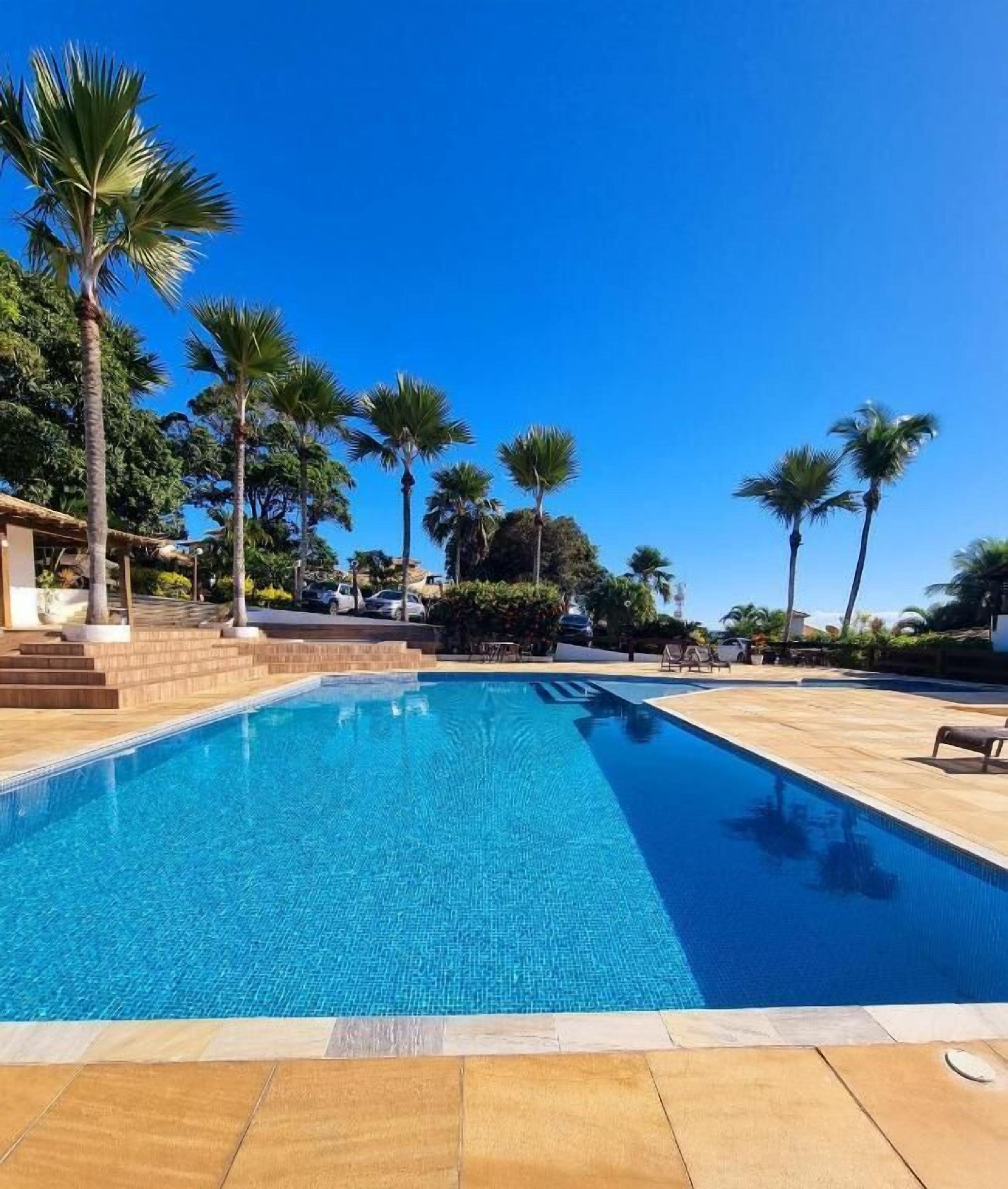 A swimming pool with clear blue water, surrounded by palm trees and a wooden deck.