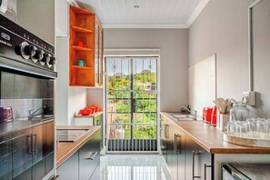 A modern kitchen with a large window, stainless steel appliances, and wooden shelves. - Serene 2-bedroom Apartment in Gqeberha With River Views (Gqeberha)