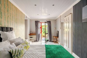 Een slaapkamer met een bed, een groen vloerkleed, een dressoir, een stoel en een deur naar buiten.