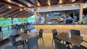 Een terrasrestaurant met tafels en stoelen, een keuken en uitzicht op groen.