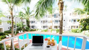 Een balkon met een laptop, een koffiekop, croissants en een glas sinaasappelsap.