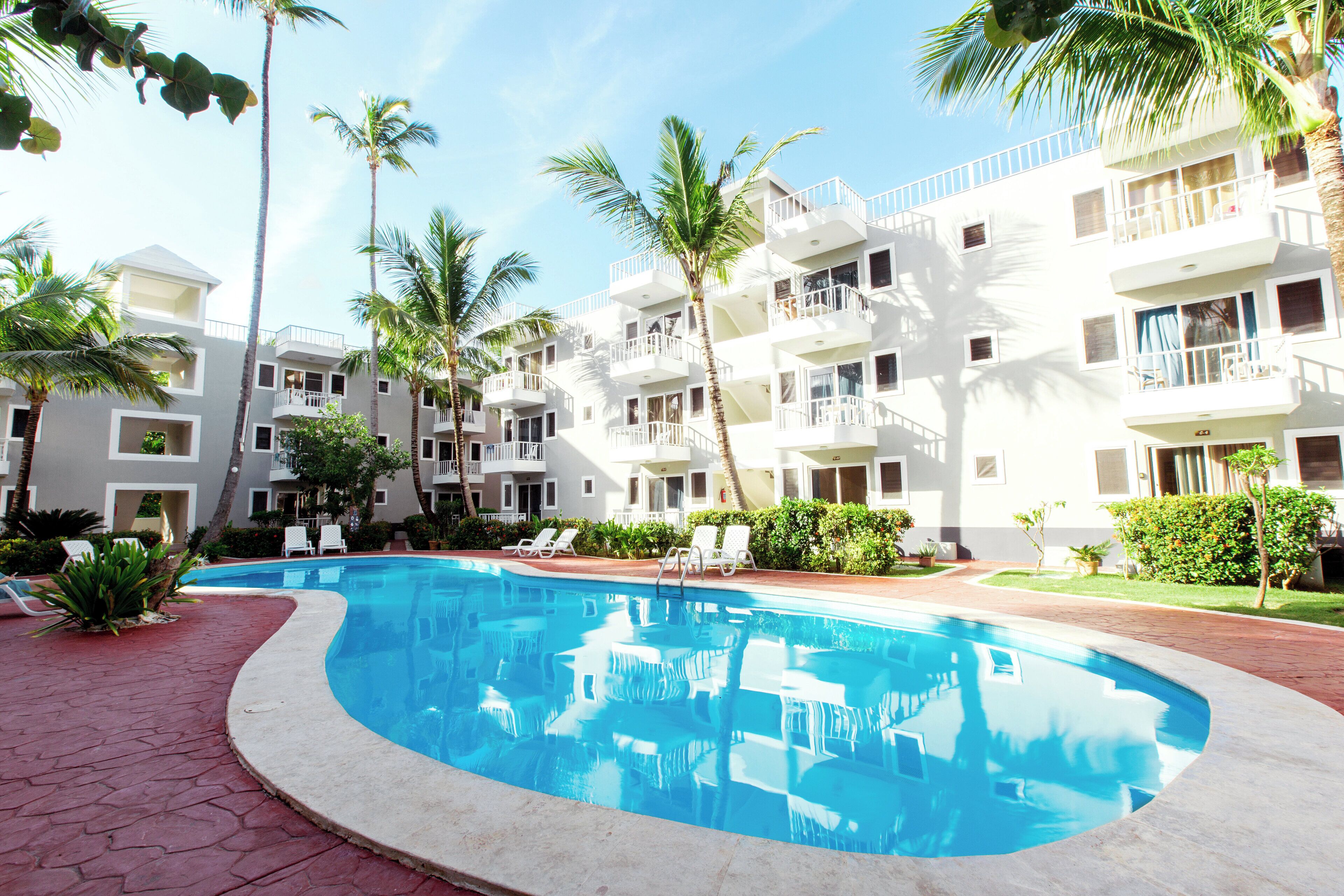 A hotel with a swimming pool, multiple balconies, and palm trees.