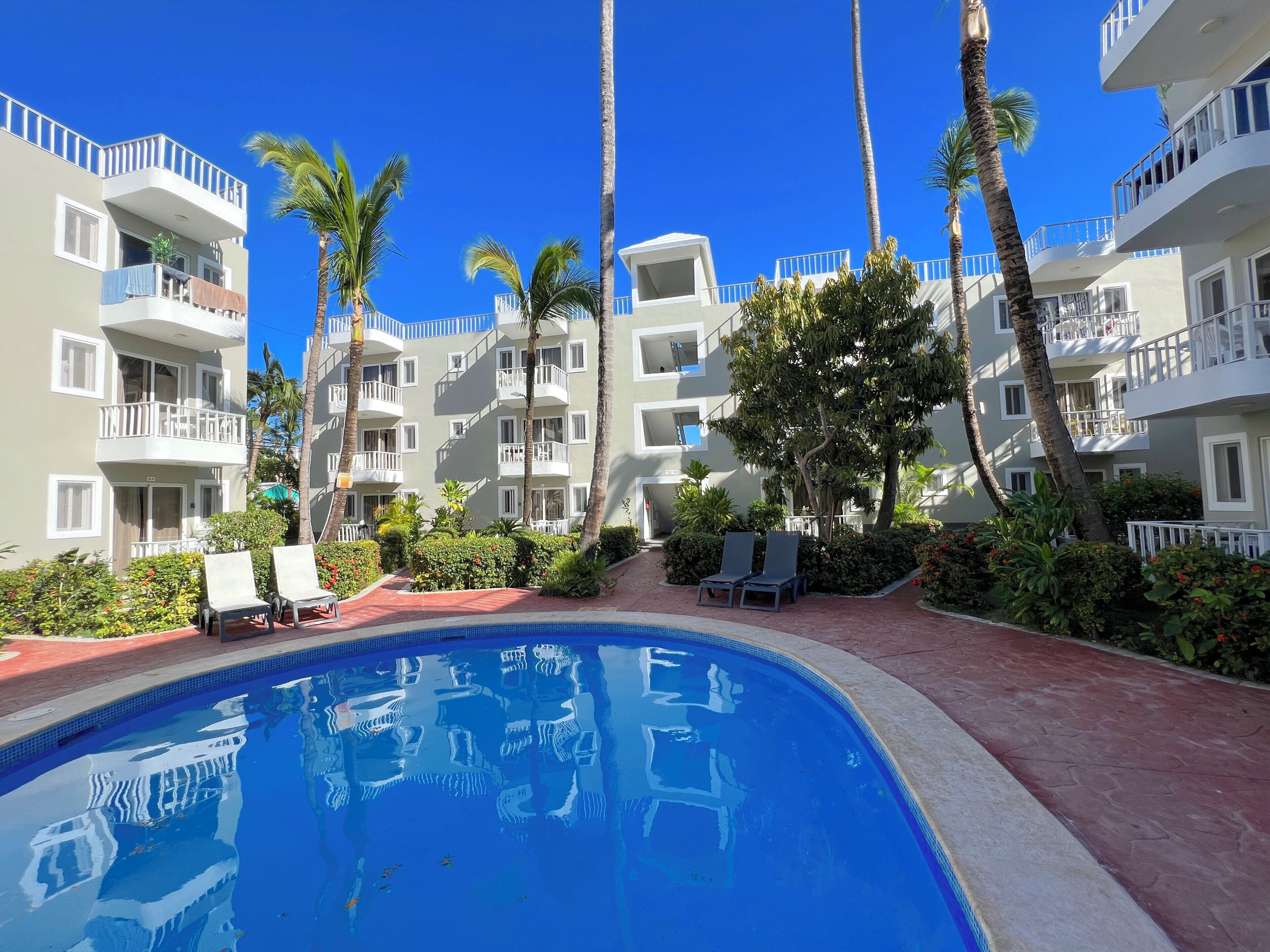 A pool surrounded by palm trees and a building with balconies.