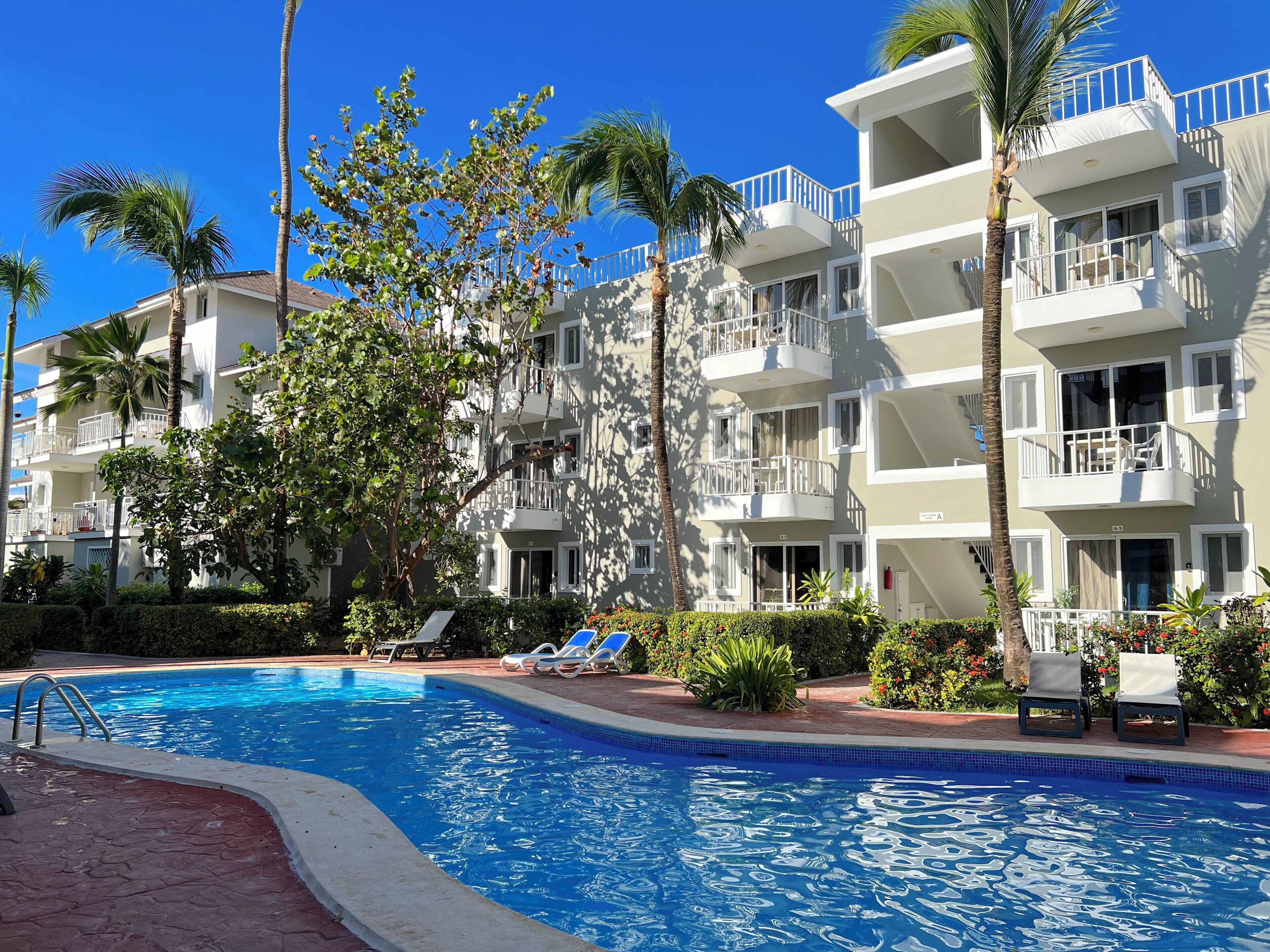 A multi-story hotel with balconies, a swimming pool, and palm trees.