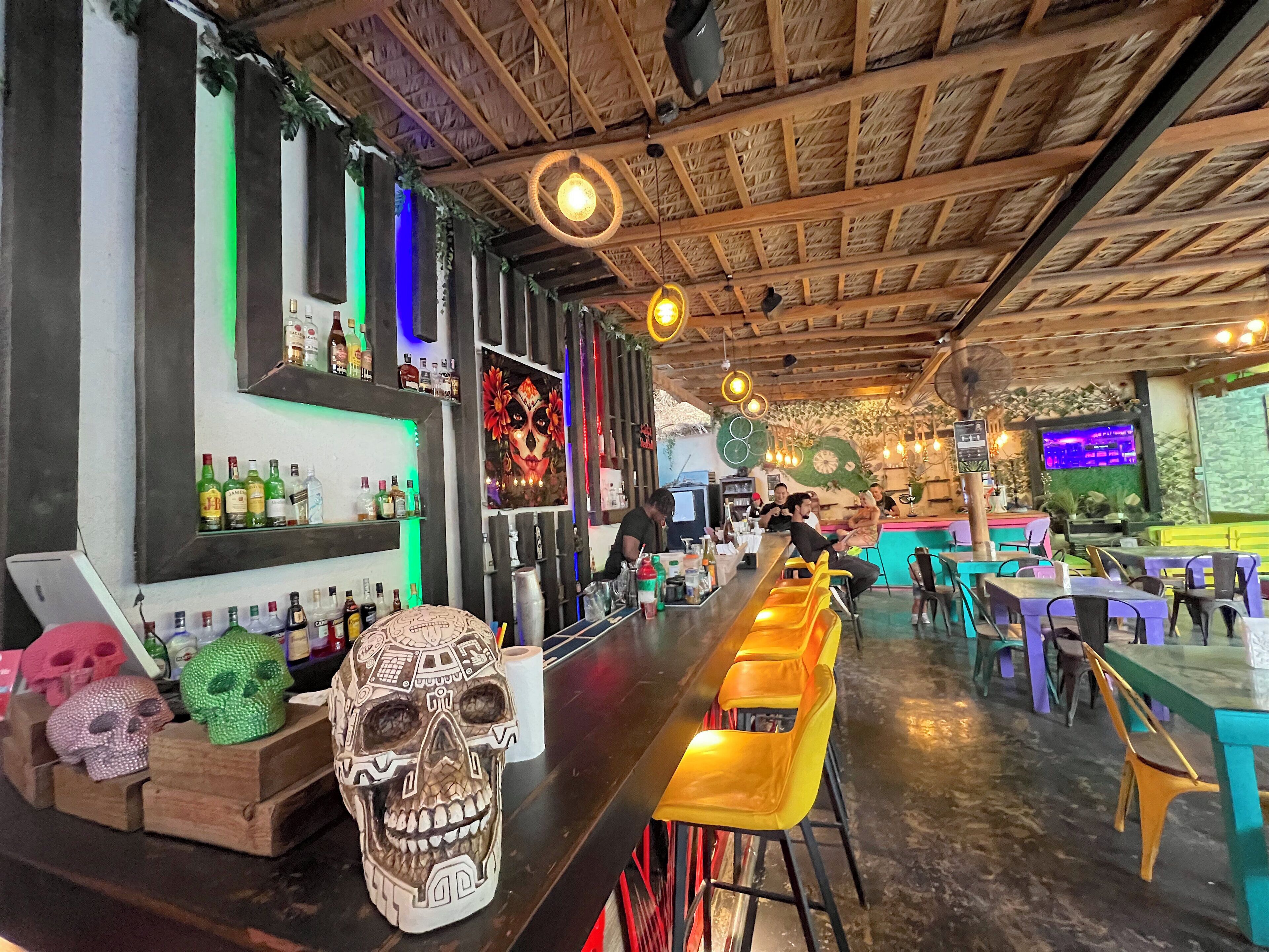 A bar area with a wooden ceiling, shelves with bottles, a skull decoration, and a bar counter.