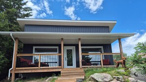 A modern two-story house with a wooden deck, a front door, and a staircase leading to the entrance. - Northern Paradise on the lake with water activities, Pet-friendly (Hagar)