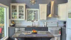 A modern kitchen with a central island, bar stools, a built-in oven, and a window overlooking greenery. - Northern Paradise on the lake with water activities, Pet-friendly (Hagar)
