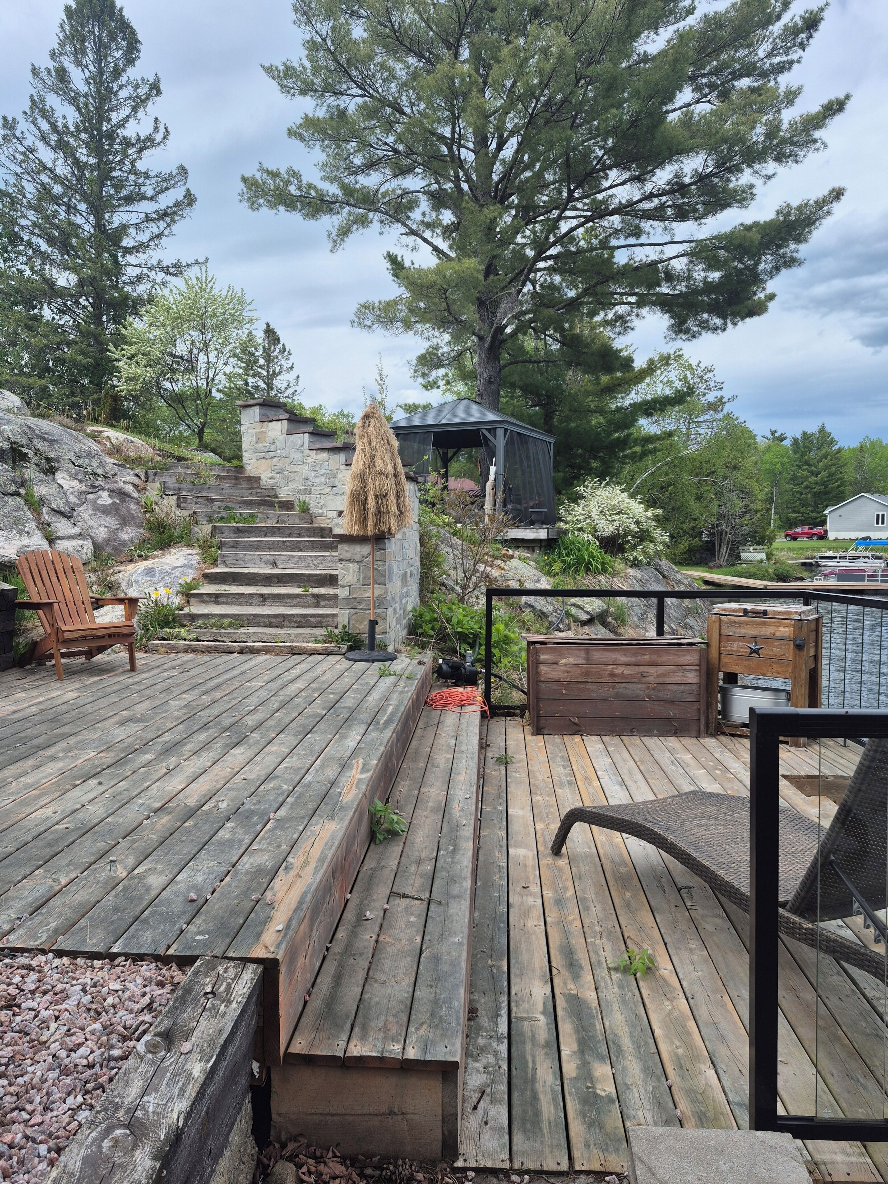 A wooden deck with a stone wall, a wooden chair, a gazebo, and a large tree.. Northern Paradise on the lake with water activities, Pet-friendly