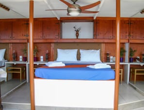 Ein Zimmer mit einem Bett, Holzschränken, einem Deckenventilator und einer Vase mit Blumen.