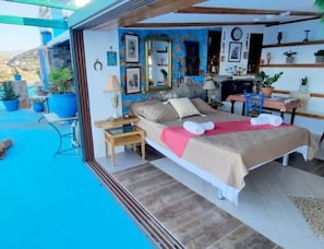 A bedroom with a bed, bedside tables, a mirror, and a view of the outdoors. - Seaside Ntounas Apartments - Cretan Double Nest (Agios Nikolaos)
