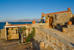 A stone building with a tiled roof overlooking a body of water. - Seaside Ntounas Apartments - Cretan Double Nest (Agios Nikolaos)