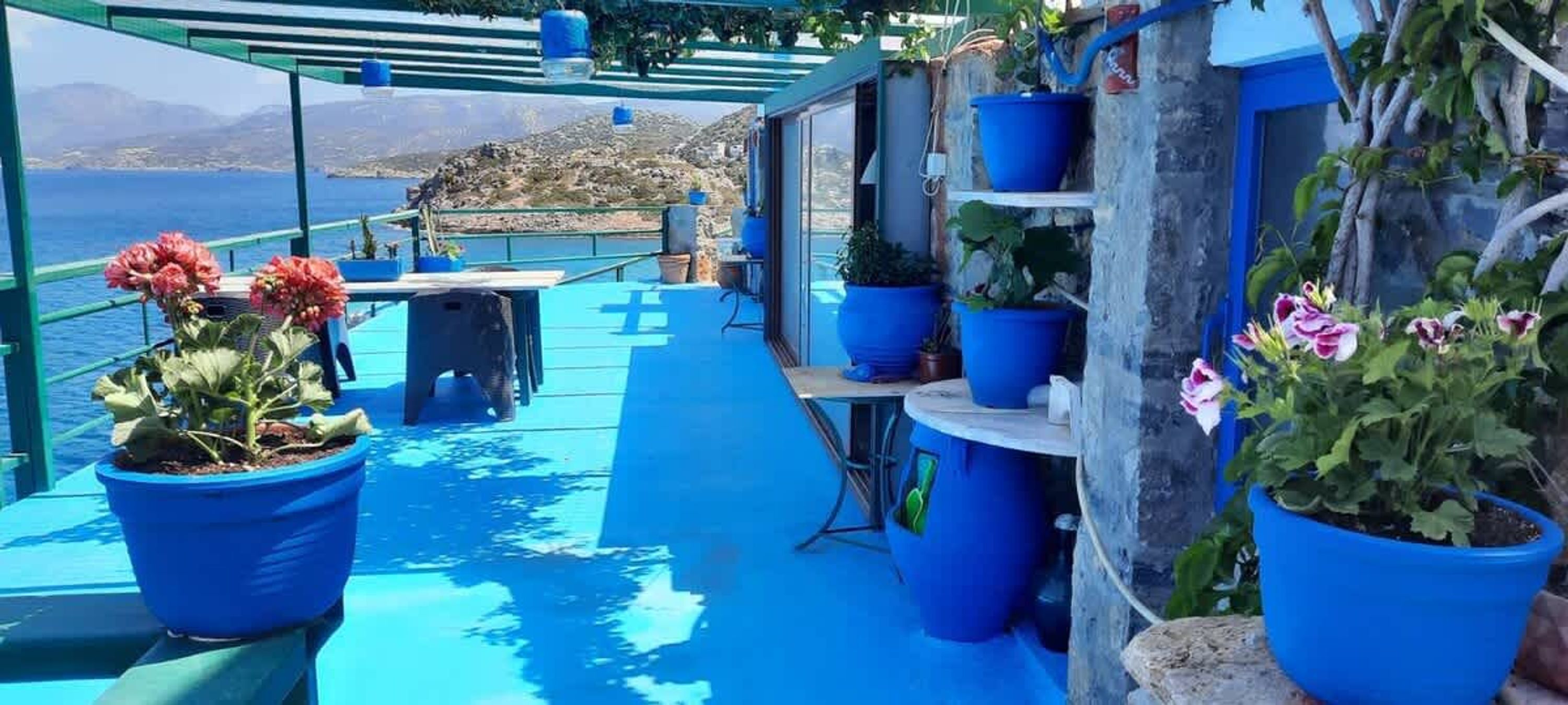 En blå dækket terrasse med plantekasser, et bord og udsigt til havet og bakker.