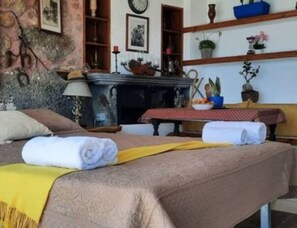 Una habitación con una cama, una mesa con mantel rojo y estantes con objetos decorativos.