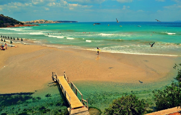 A beach with clear water, a wooden pier, and a distant cityscape. - Seaside Ntounas Apartments - Cretan Double Nest (Agios Nikolaos)