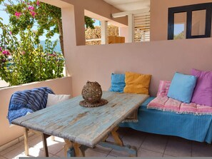 A cozy outdoor seating area with a wooden table, cushions, and a decorative vase. - Votsalon Beach House - Sea View Hideaway Zakynthos (Zakynthos)