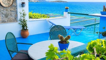 A terrace with a view of the sea, a table, chairs, and potted plants.