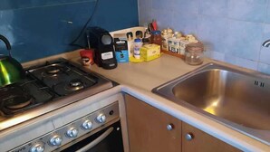 Eine kleine Küche mit einem Gaskochfeld, einem Spülbecken und diversen Küchenutensilien auf der Arbeitsfläche.