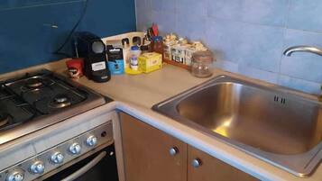 A compact kitchen with a gas stove, a sink, and various kitchen items on the countertop.