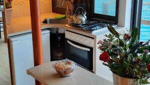 A kitchen with a stove, sink, and window overlooking the sea. - Seaside Ntounas Apartments - Ammoudara Triple Gem (Agios Nikolaos)