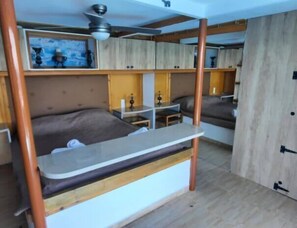 Ein kleines Zimmer mit Etagenbett, Schreibtisch und Deckenventilator.