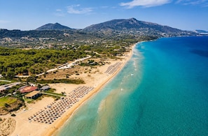 An aerial view of a coastal area with a beach, buildings, and a mountain in the background. - Votsalon Beach House - Family Retreat Zakynthos (Zakynthos)