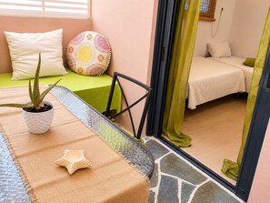 Ein Zimmer mit einem Bett, einem kleinen Tisch mit Topfpflanze, einem Zierkissen und Blick durch eine Glastür.