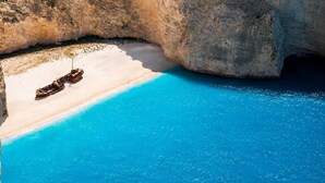 A beach with clear blue water, a sandy shore, and a boat. - Votsalon Beach House - Gem for 2 in Zakynthos (Zakynthos)