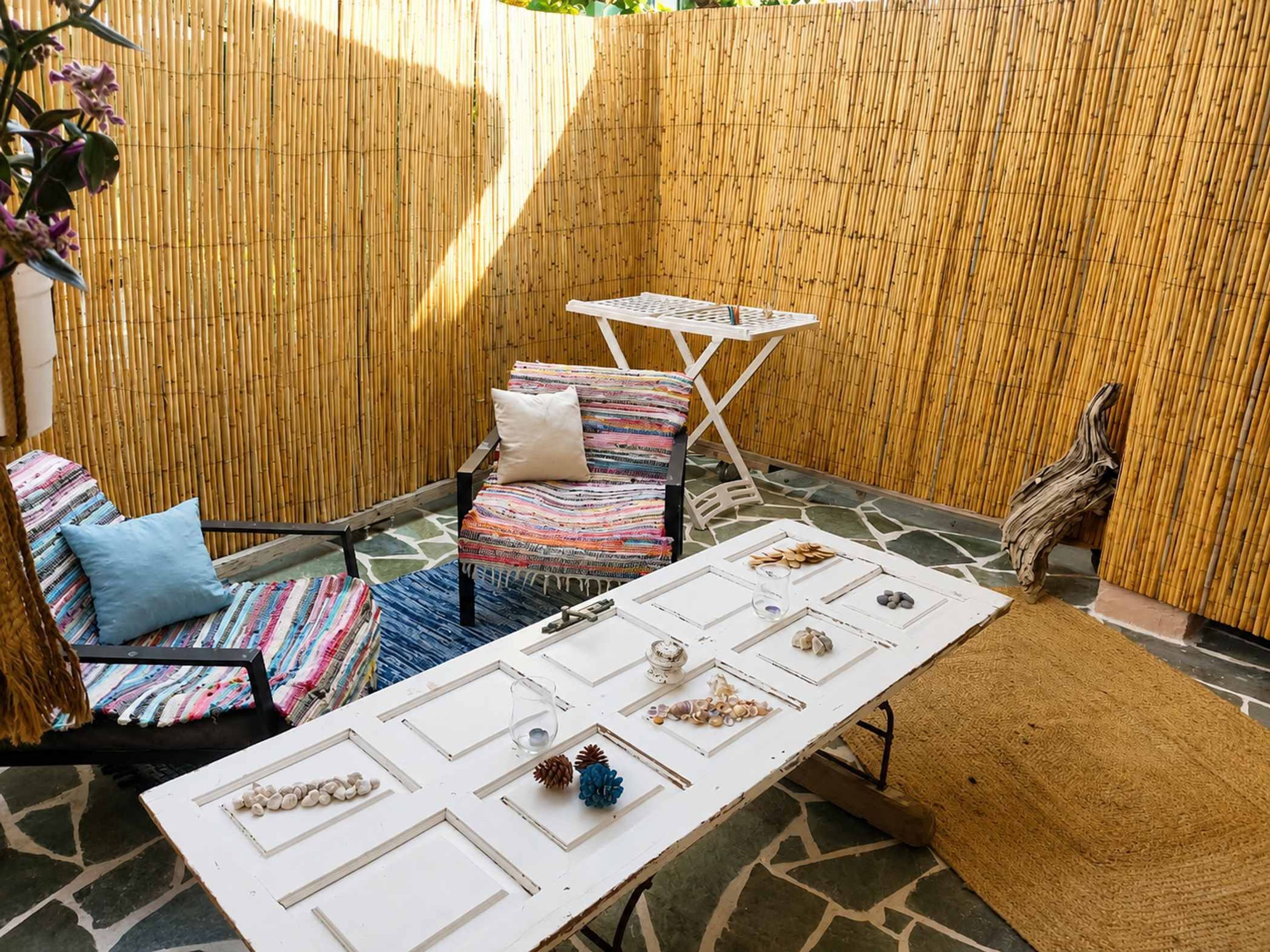 Une terrasse avec une table, des chaises et un mur en bambou.