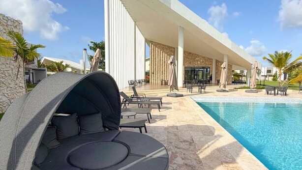 Ein moderner Poolbereich mit einer runden Lounge-Ecke, einem Pool und einer überdachten Terrasse mit Tischen und Stühlen.