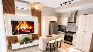 Una cocina moderna con horno integrado, un comedor con taburetes de bar, una sala de estar con sofá y un televisor que muestra una chimenea.