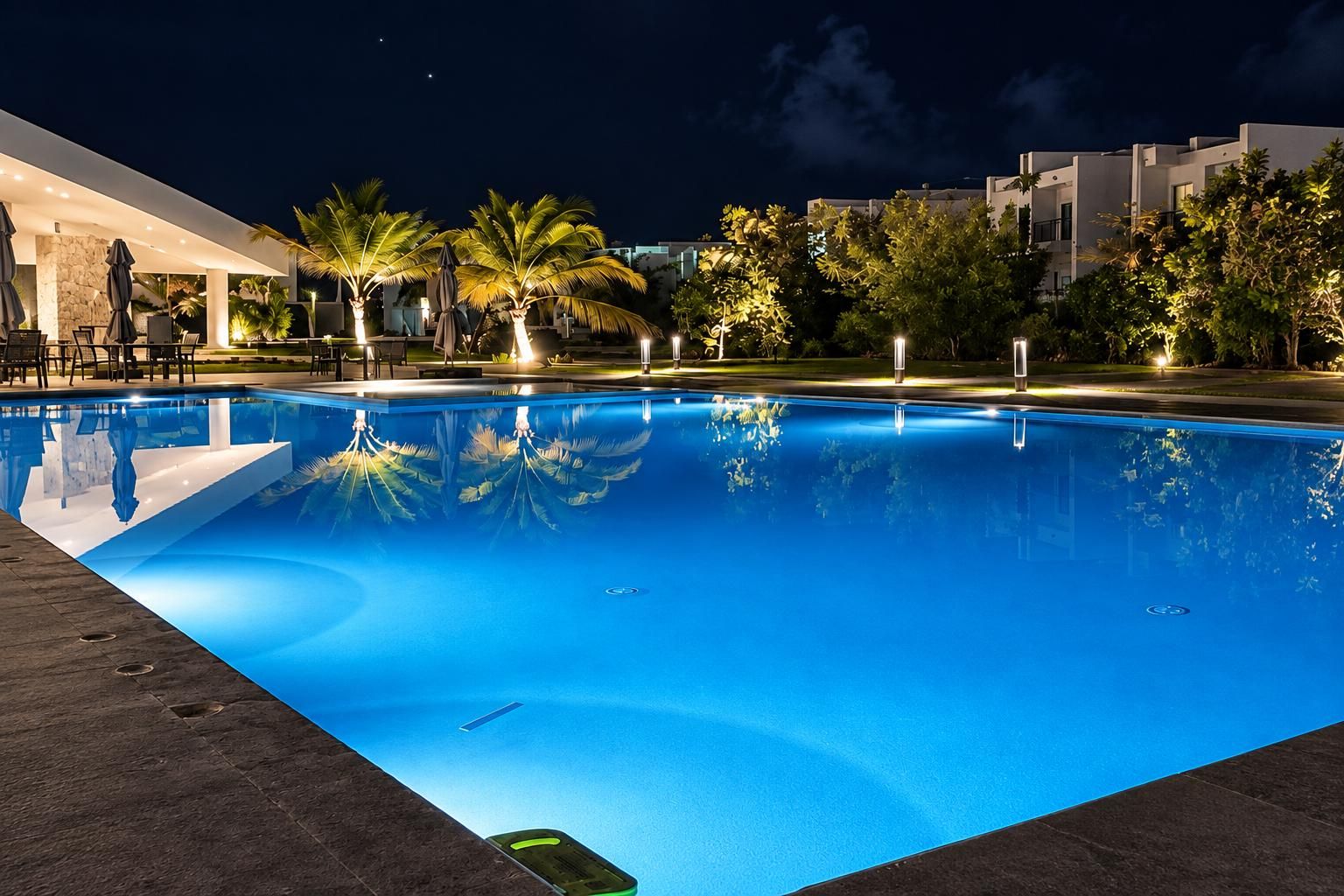A swimming pool with a clear blue surface, surrounded by palm trees and outdoor seating.